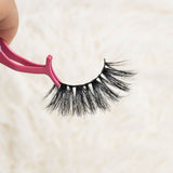 Mink eyelashes held with pink applicator showcasing thick volume and curl.